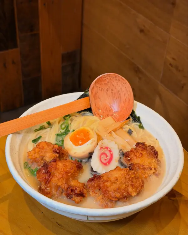 Tonkotsu ramen with crispy karaage chicken, a jammy egg, menma and narutomaki, a wooden ladle resting on the bowl