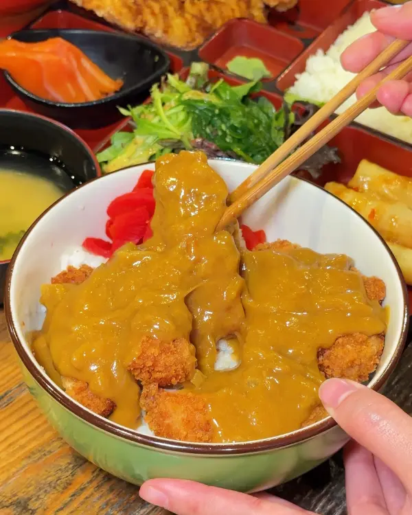 Chicken katsu curry: crumbed chicken under Japanese curry on rice, chopsticks lifting a piece