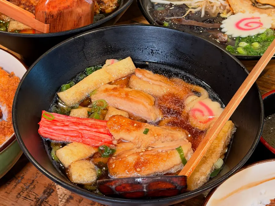 Teriyaki chicken udon, karaage and katsu on a timber table, wooden ladles in the bowls